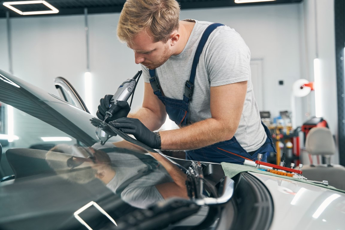A picture of a man doing glass repair on a car windshield